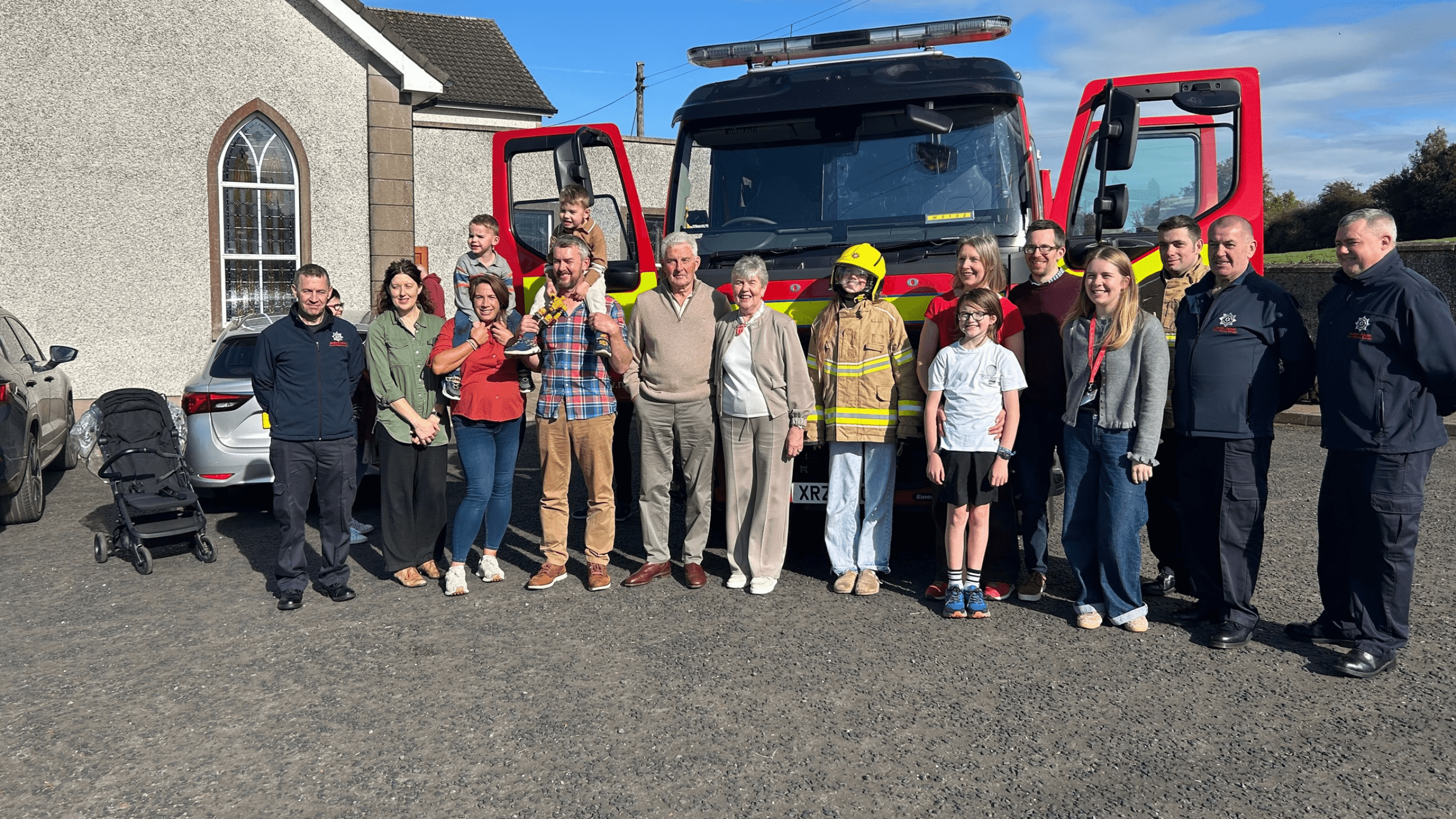 A group of adults and children posing for a photo in front of a parked fire engine.
