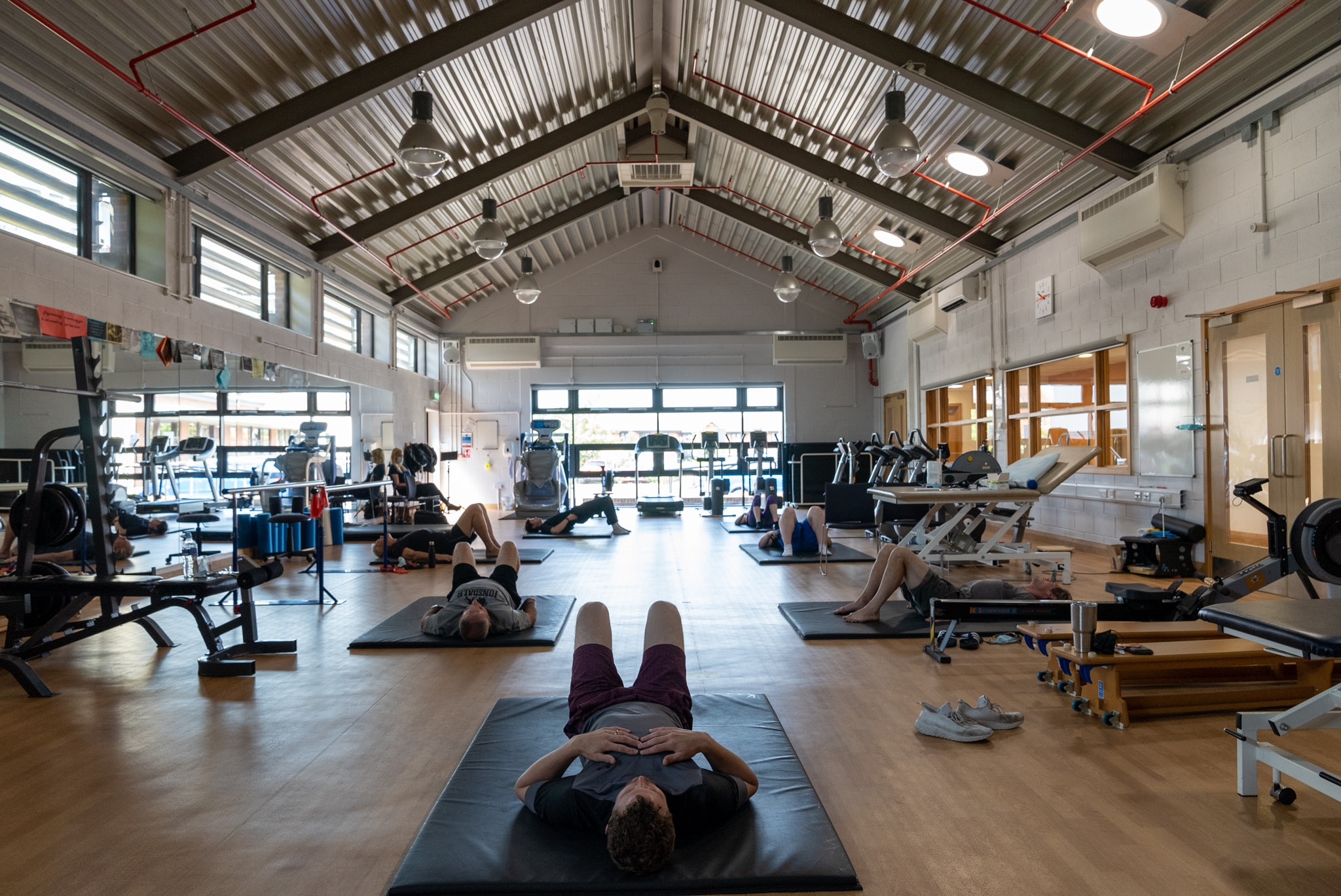 a wide angled shot of a Fire FIghters Charity gym, showing a number of service users lying on gym mats on the floor 