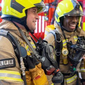 Two London firefighter in full kit laughing during training.