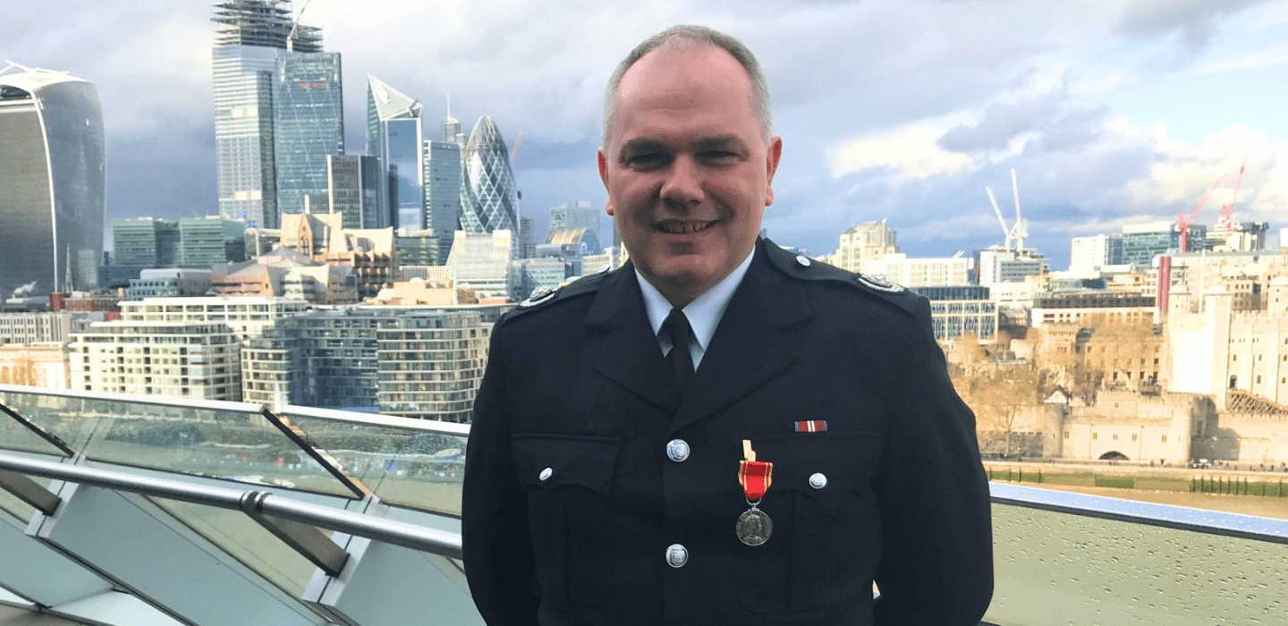A portrait of Steve Norman, a former Deputy Assistant Commissioner for London Fire Brigade, smiling in an outdoor setting. in front of the London city skyline.
